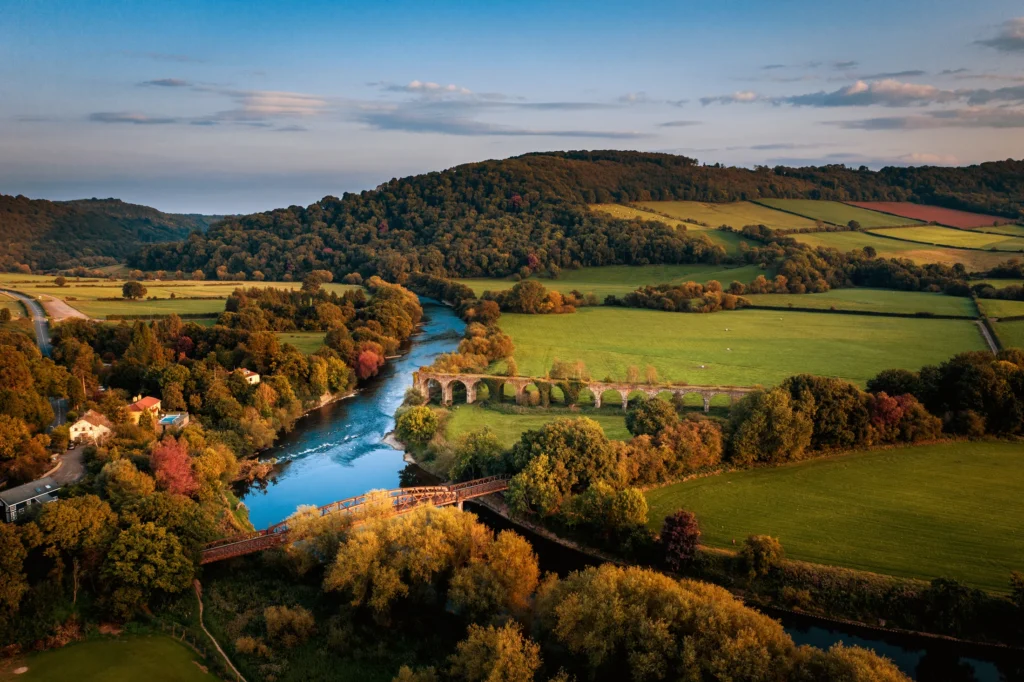 The River Wye winding through woodland and fields beside an old stone viaduct.