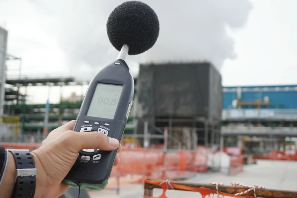 A handheld sound level meter measuring noise at an industrial site.