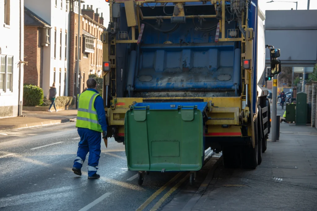 A refuse collection worker moving a large wheeled bin to a collection vehicle.