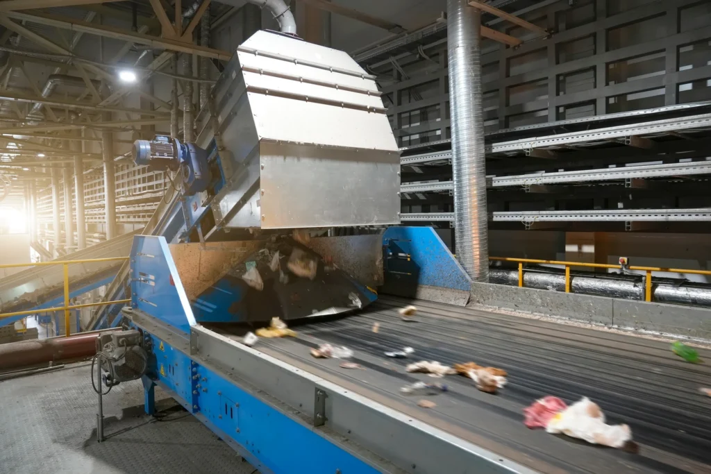 Mixed waste passing through conveyor and sorting equipment inside a processing facility.