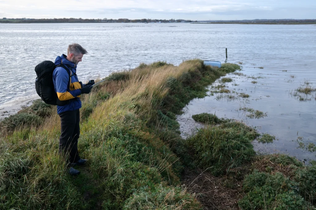 An ecologist recording field notes beside a salt marsh.